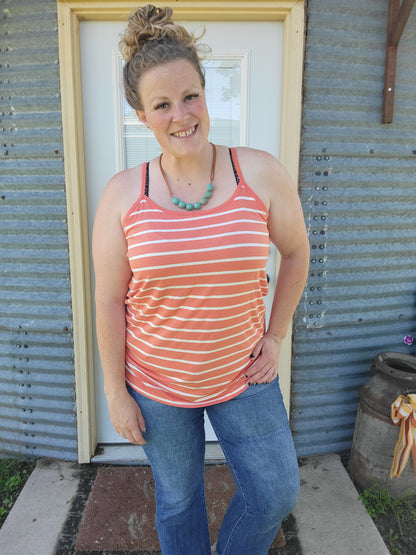 Woman wearing a striped tank top and jeans standing in front of a corrugated metal building.