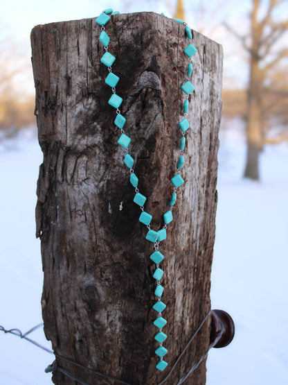 Turquoise beaded necklace draped over a wooden post with a snowy background