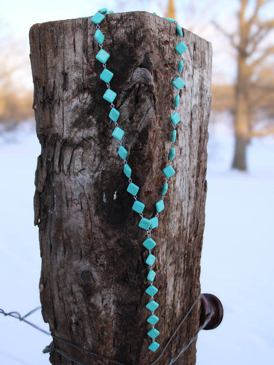 Turquoise beaded necklace draped over a wooden post with a snowy background